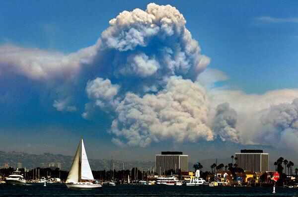 A sailboat makes its way through the harbor in Marina del Rey against a backdrop of smoke from the Station fire.