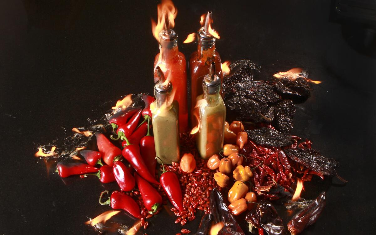 An array of hot chile peppers and bottles of hot sauces made with them. (Kirk McKoy / Los Angeles Times)