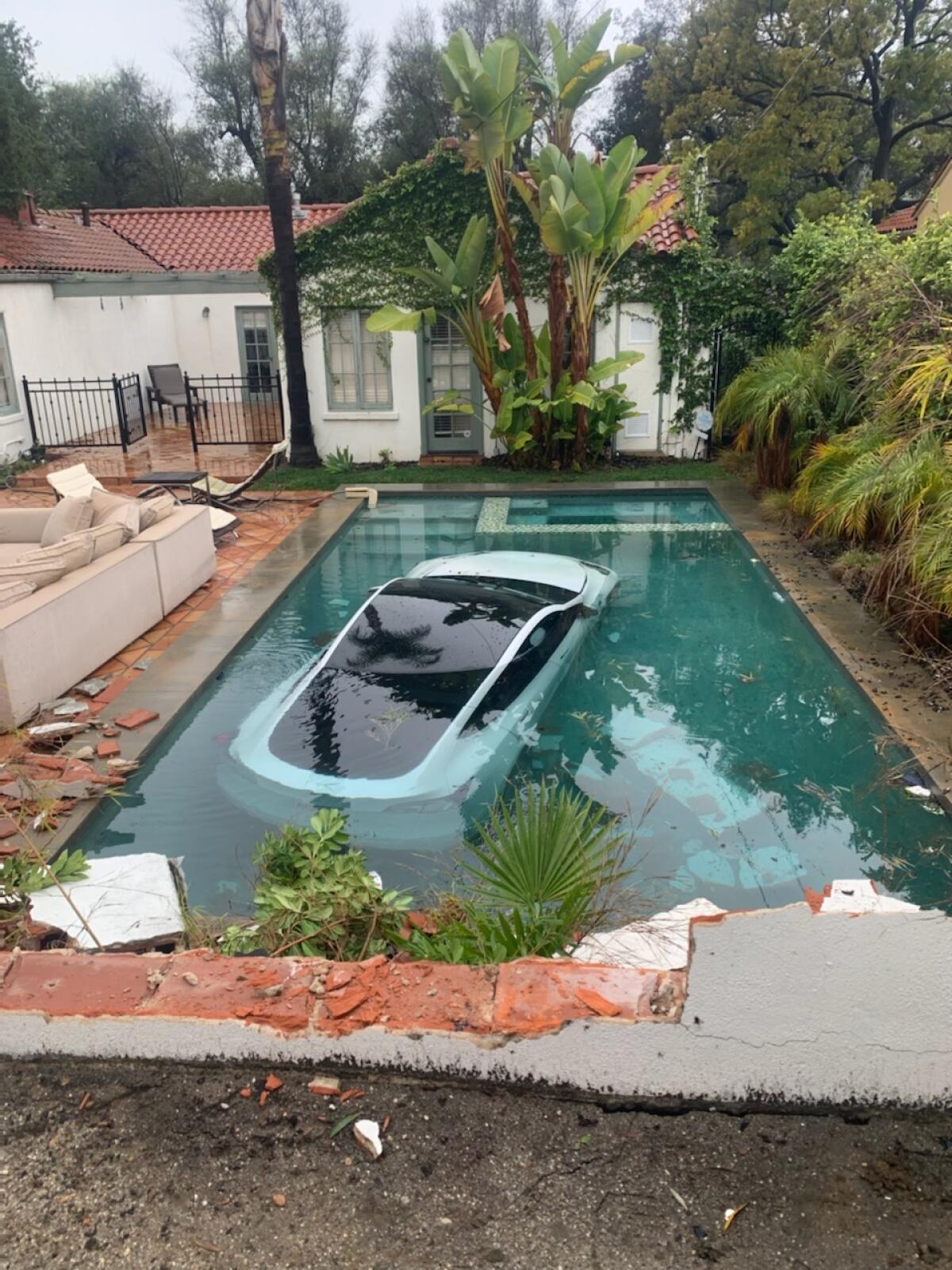 A white Tesla car sits submerged in a pool in a backyard. 