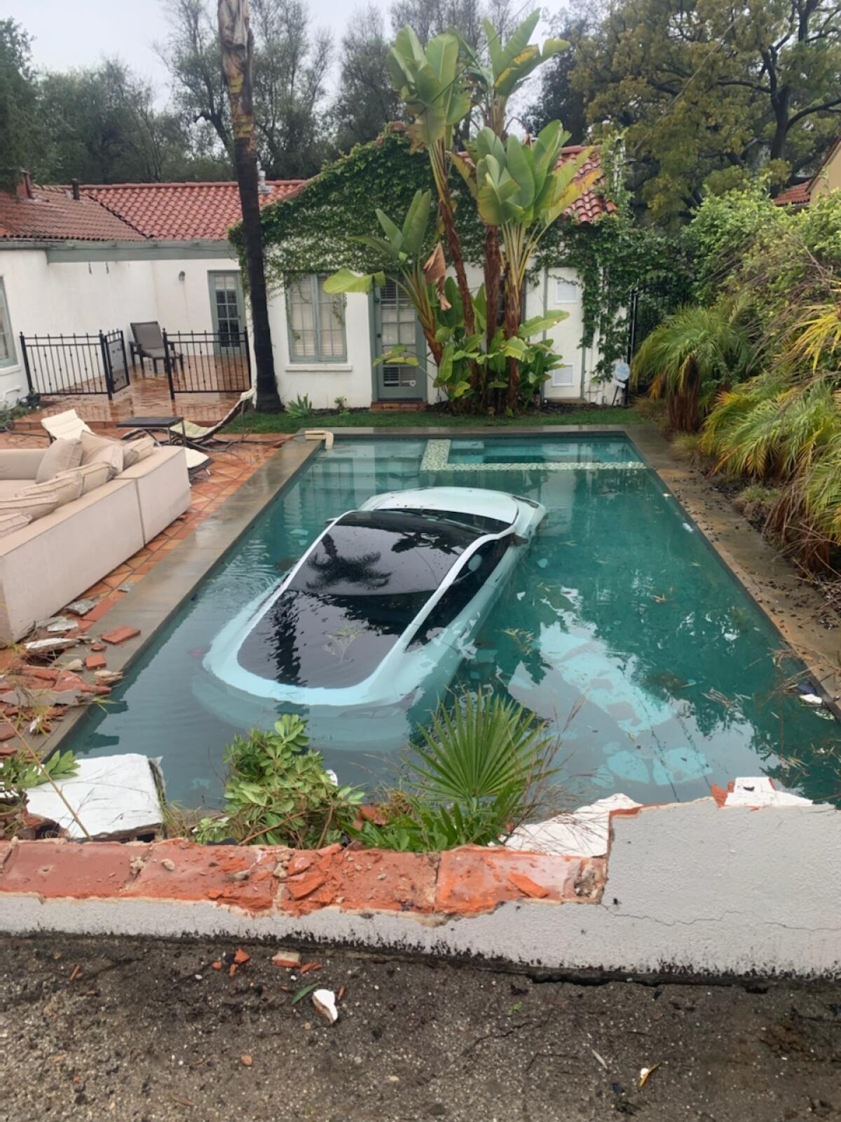 A white Tesla car sits submerged in a pool in a backyard.