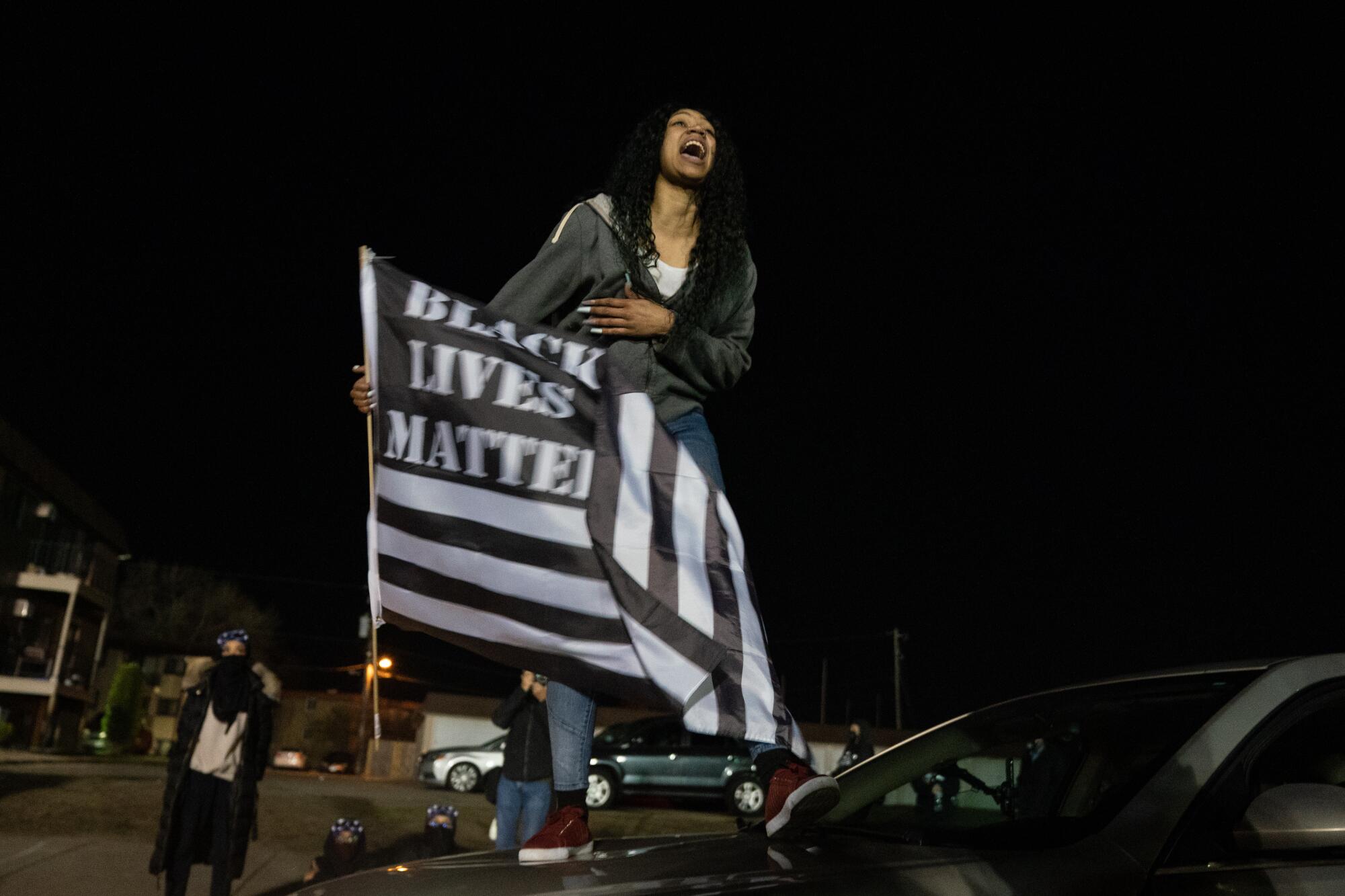 A protester stands on the hood of her car holding a Black Lives Matter flag outside the Brooklyn Center Police Department