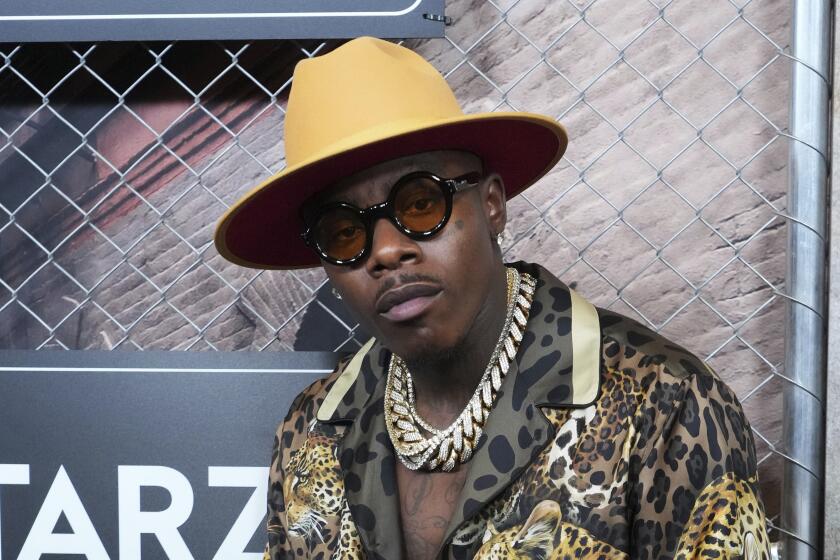 A man in a hat, glasses, gold chains and an animal-print jacket