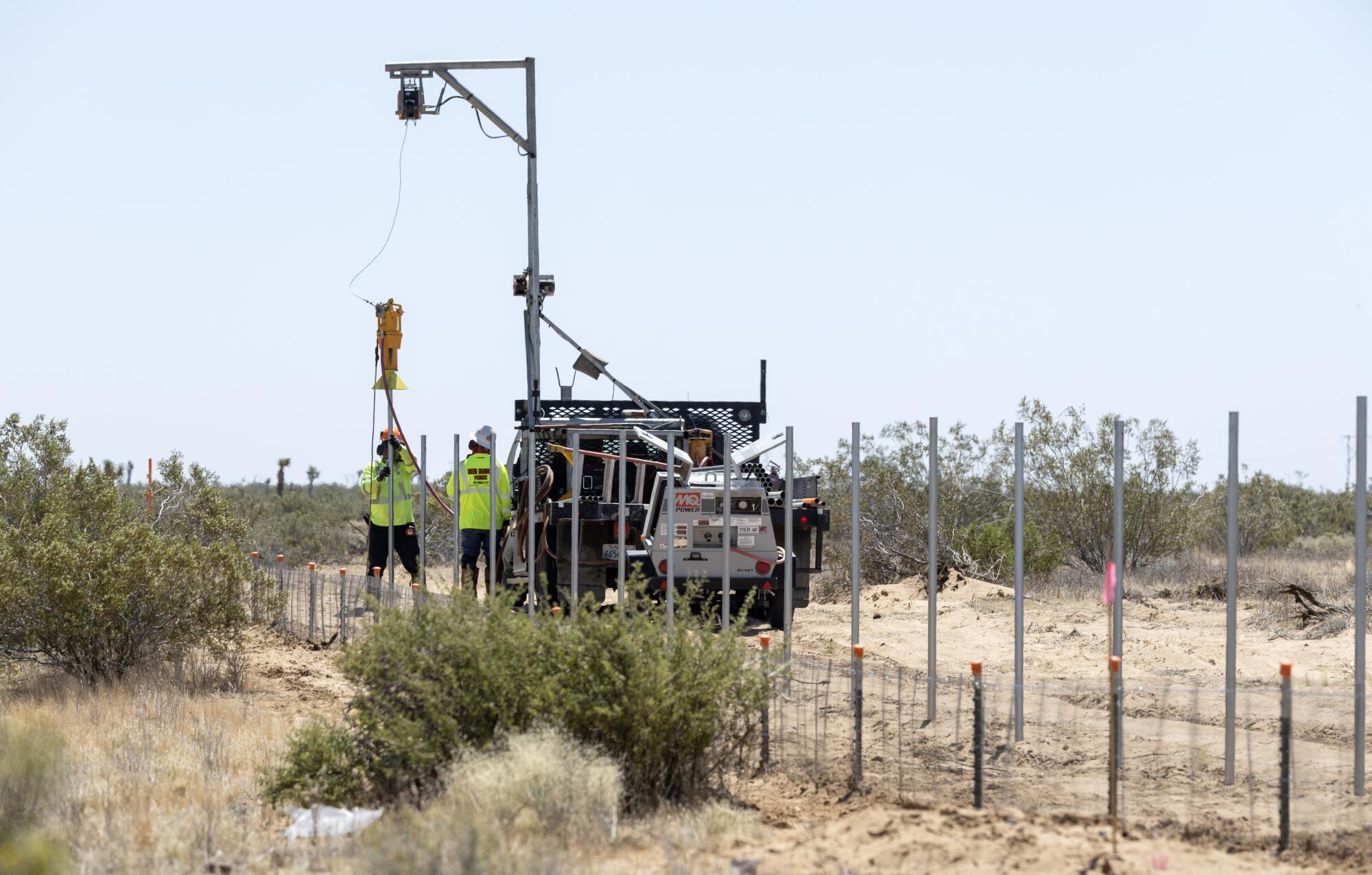 Workers install a fence amid high desert scrub.