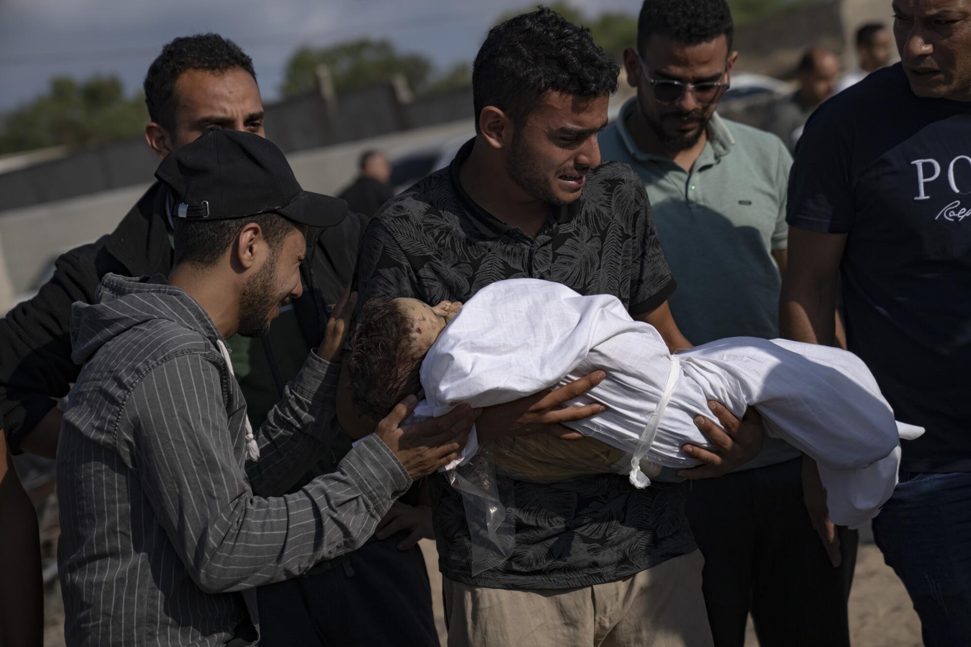 Man holding wrapped body of young relative killed in Israeli airstrike