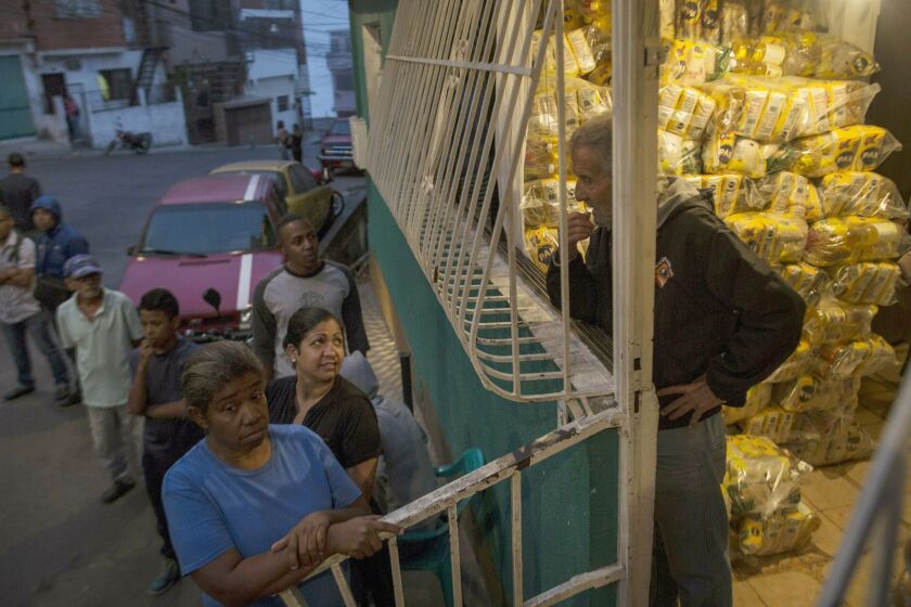 Neighbors wait to receive bags of subsidized food distributed under a government program named "CLAP, " in the Catia district of Caracas, Venezuela, Thursday, Jan. 31, 2019. An independent U.N. human rights monitor says economic sanctions are compounding a "grave crisis" in Venezuela. (AP Photo/Rodrigo Abd)