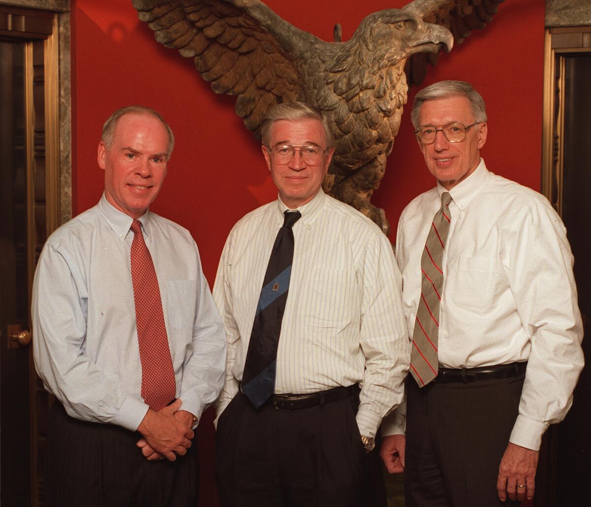 Three men in dress shirts and ties in front of a statue of an eagle.
