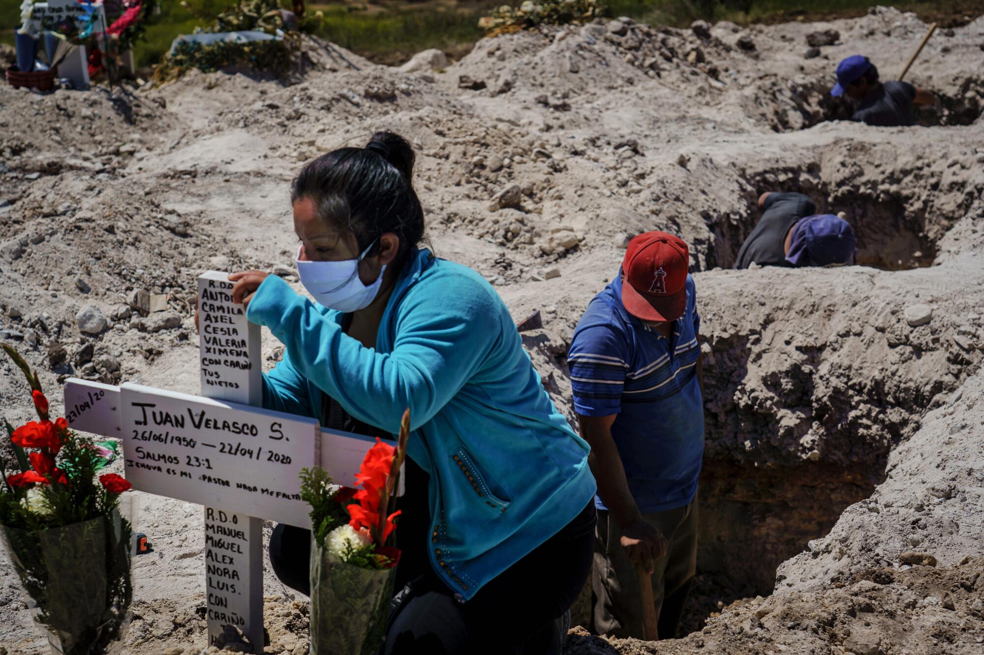 At Tijuana's Municipal Cemetery No. 13, Nora Lassete marks the burial cross after the funeral of Juan Velasco, who died of COVID-19 symptoms.