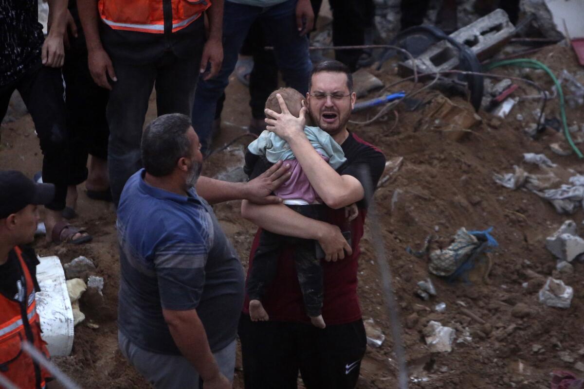 A Palestinian man cries while holding a dead child found under the rubble of a destroyed building.