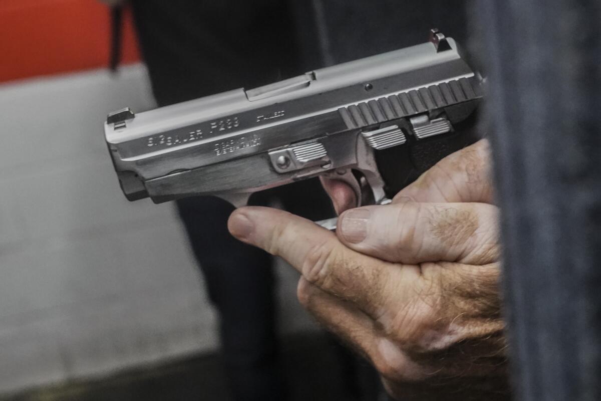 A closeup of a person's left hand bracing a silver semiautomatic handgun, their right finger on its trigger