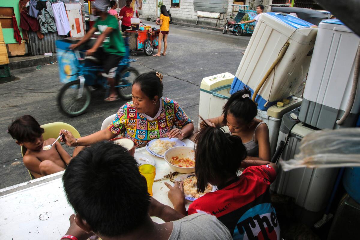Jaquelin Marsan feeds her son rice outside their home in a Manilla neighborhood called Del Pan Binondo, a slum of scavenged wood and corrugated sheet metal homes.