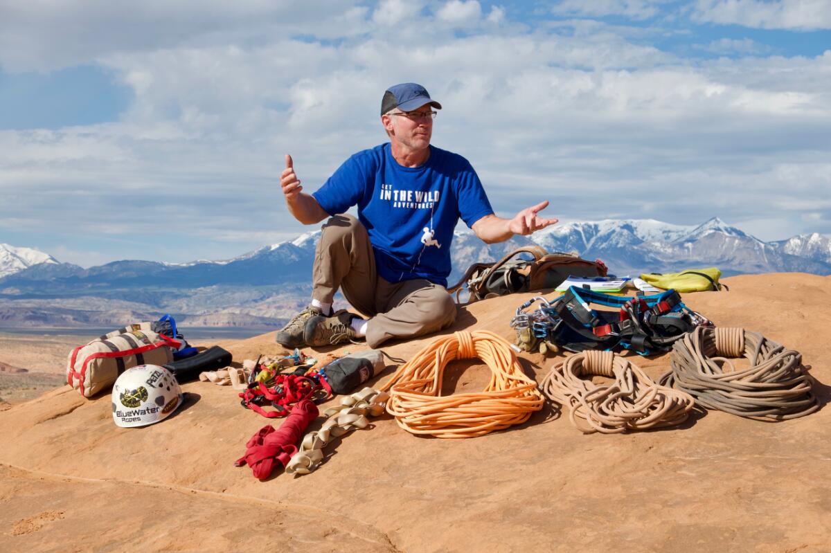 A man sits on a sand dune surrounded by climbing equipment