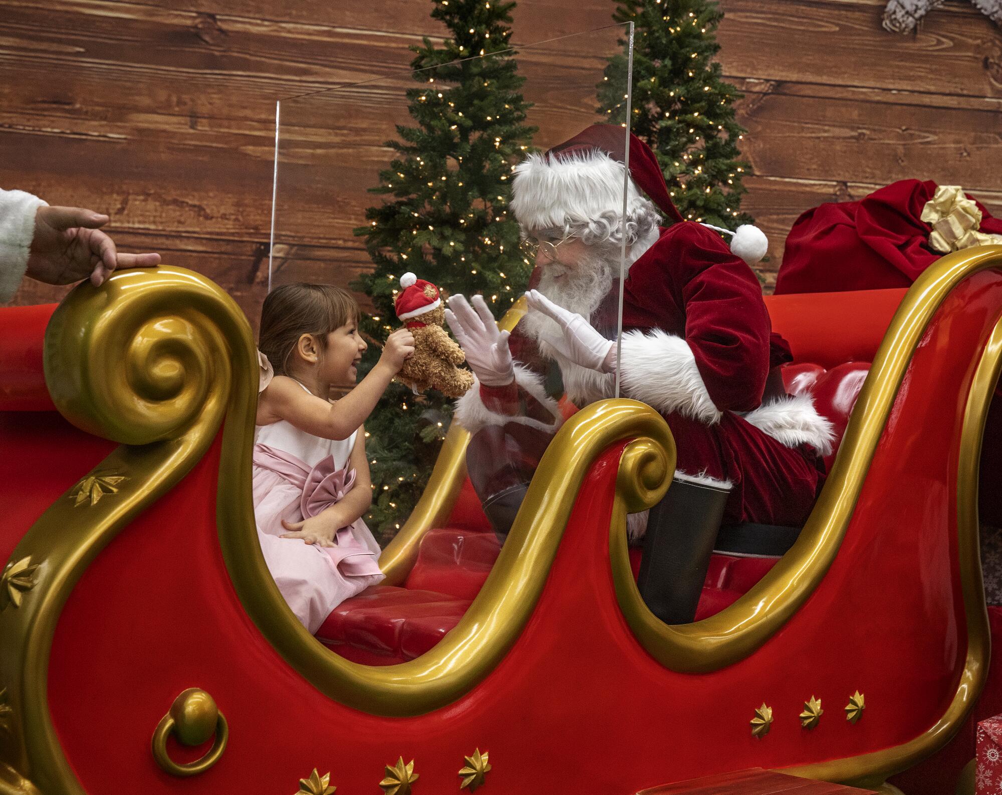 Delilah Liljedahl-Loya, 3, greets Santa Claus, seated inside his sleigh