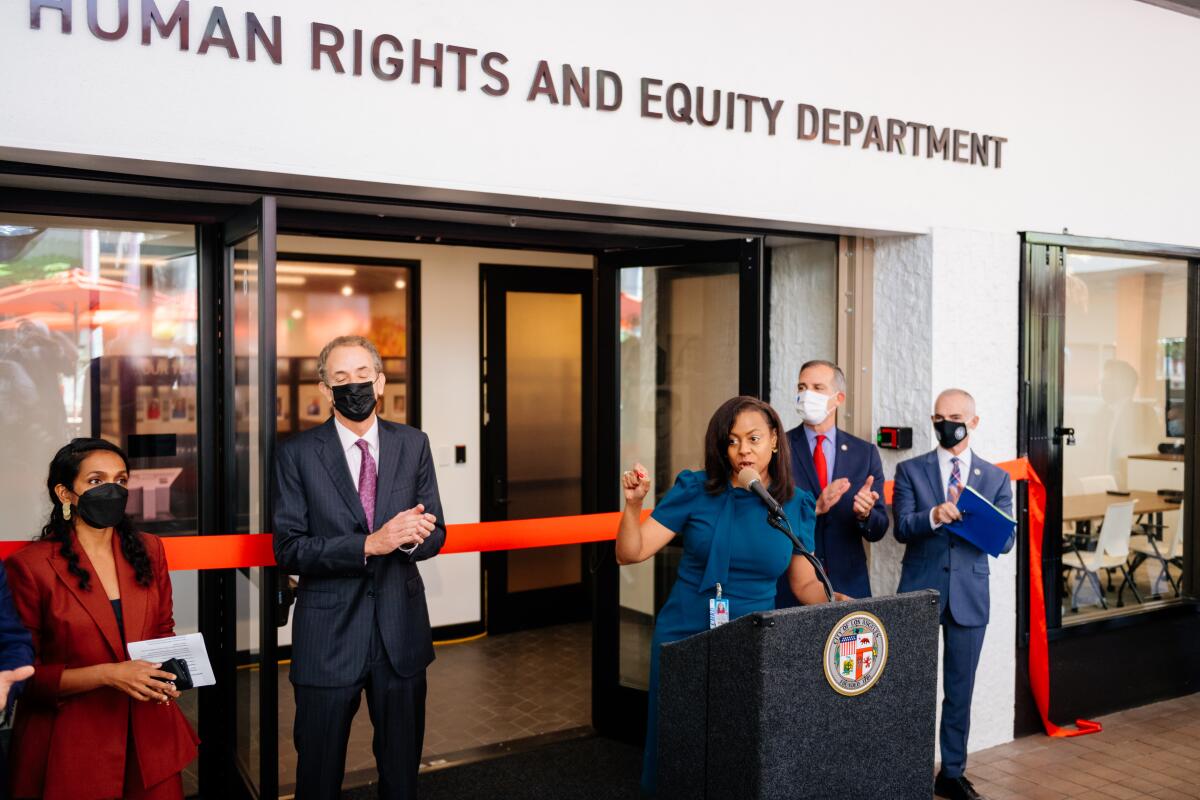 A woman is standing at a podium in front of a building with the words "Human Rights and Equity Department" on it.