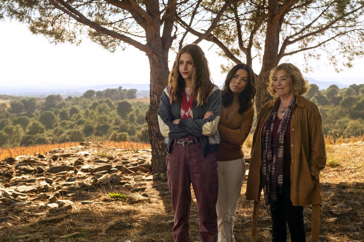 Three women standing near trees on top of a hill.