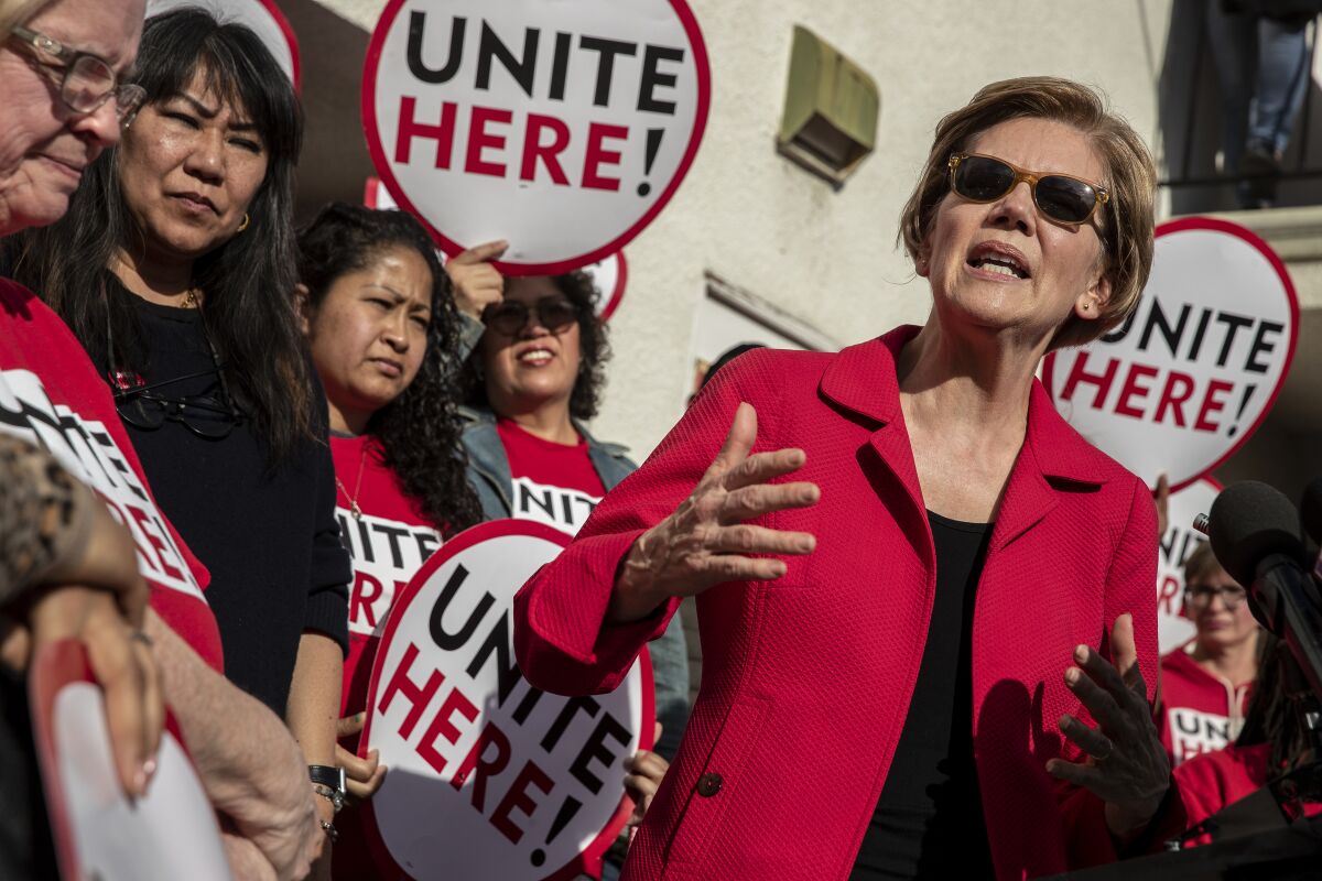 People in red shirts with "Unite Here" signs stand by Elizabeth Warren