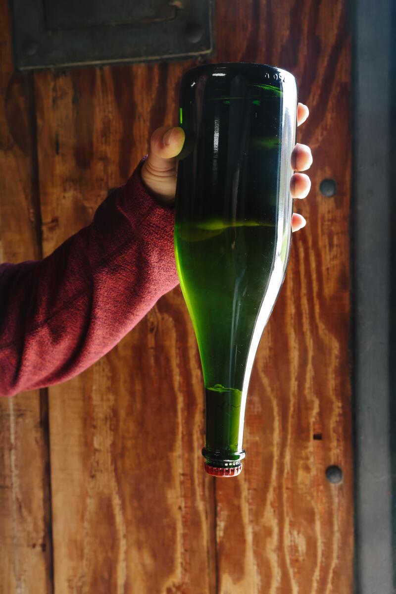 A hand holds up an upside-down wine bottle
