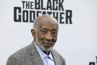 Clarence Avant stands in front of a backdrop that says 'The Black Godfather'