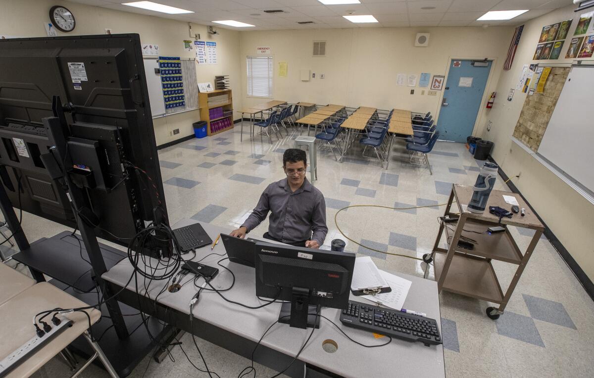 Desks are pushed to the side in a room at El Camino Real Charter High School as Manuel Velarde teaches a class online. 