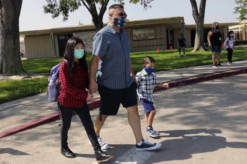 A man walks his two children in a school parking lot