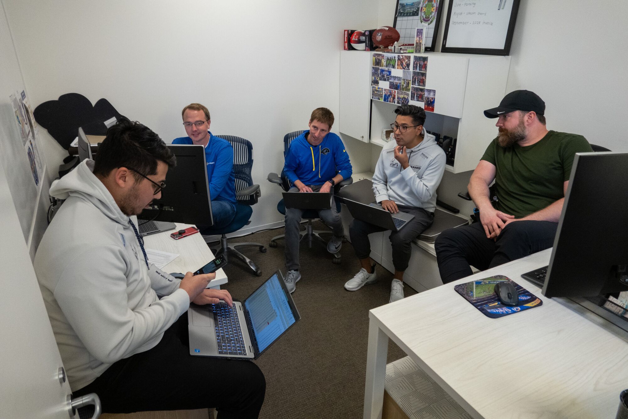 Rams employees hold a team meeting and talk while looking at computer screens.