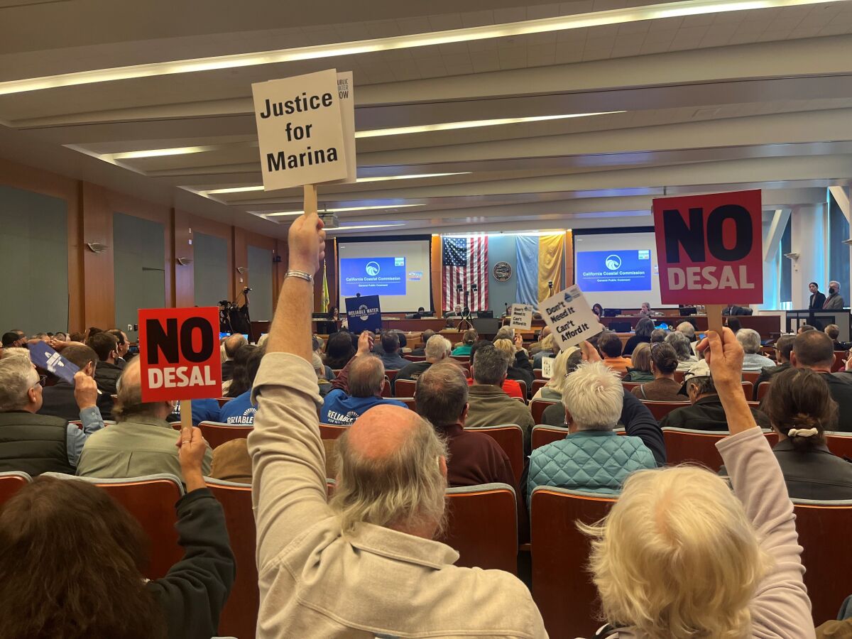 Image of crowded meeting room with people holding NO DESAL signs