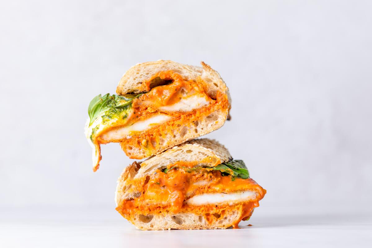 A photo of a stacked chicken cutlet sandwich oozing cheese, fresh basil and vodka sauce