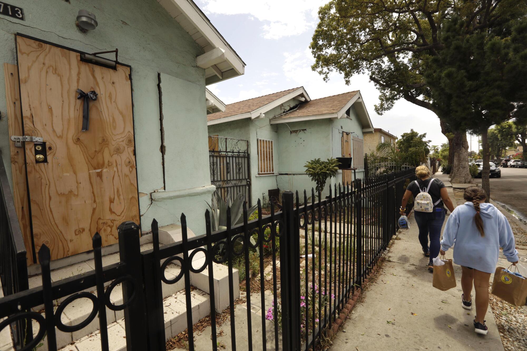 Two people walk past boarded up homes