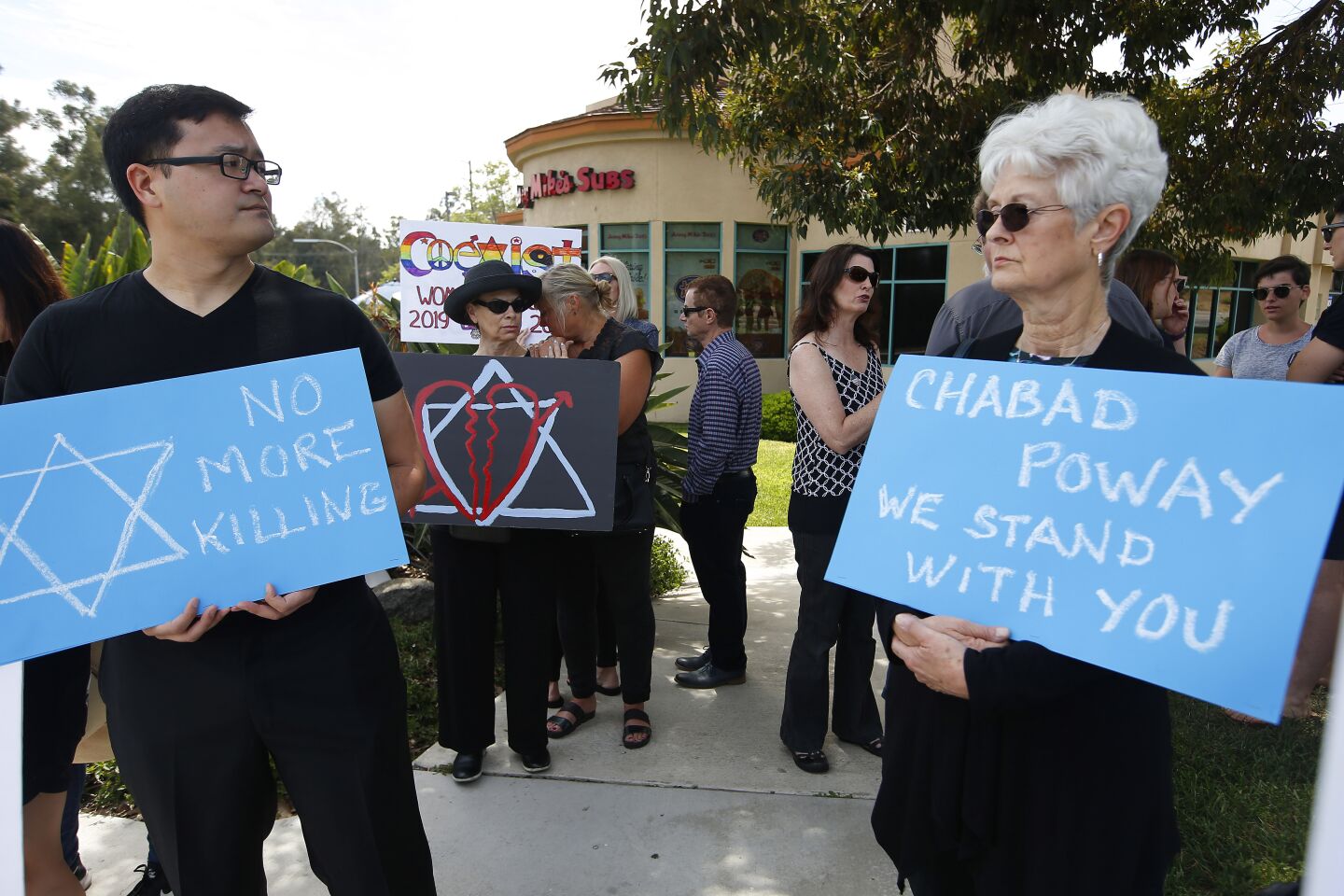 Mike Sakasegawa, left, of Mira Mesa and Penny Ribnik of Poway hold signs at a rally in support of the Jewish community not far from the Chabad of Poway, where a deadly shooting took place the day before on April 28, 2019 in Poway, California.
