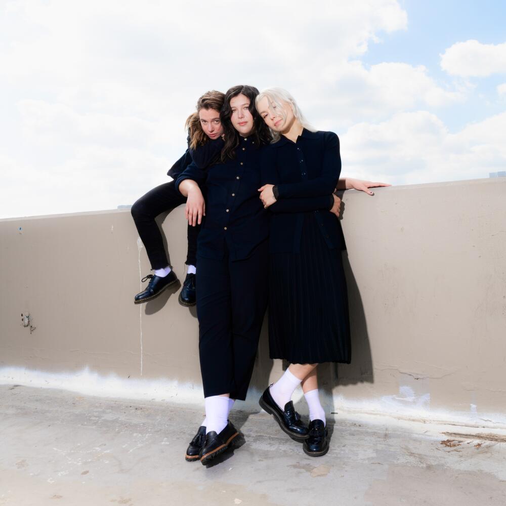 Three female rock musicians wearing black pose for a photo on a rooftop