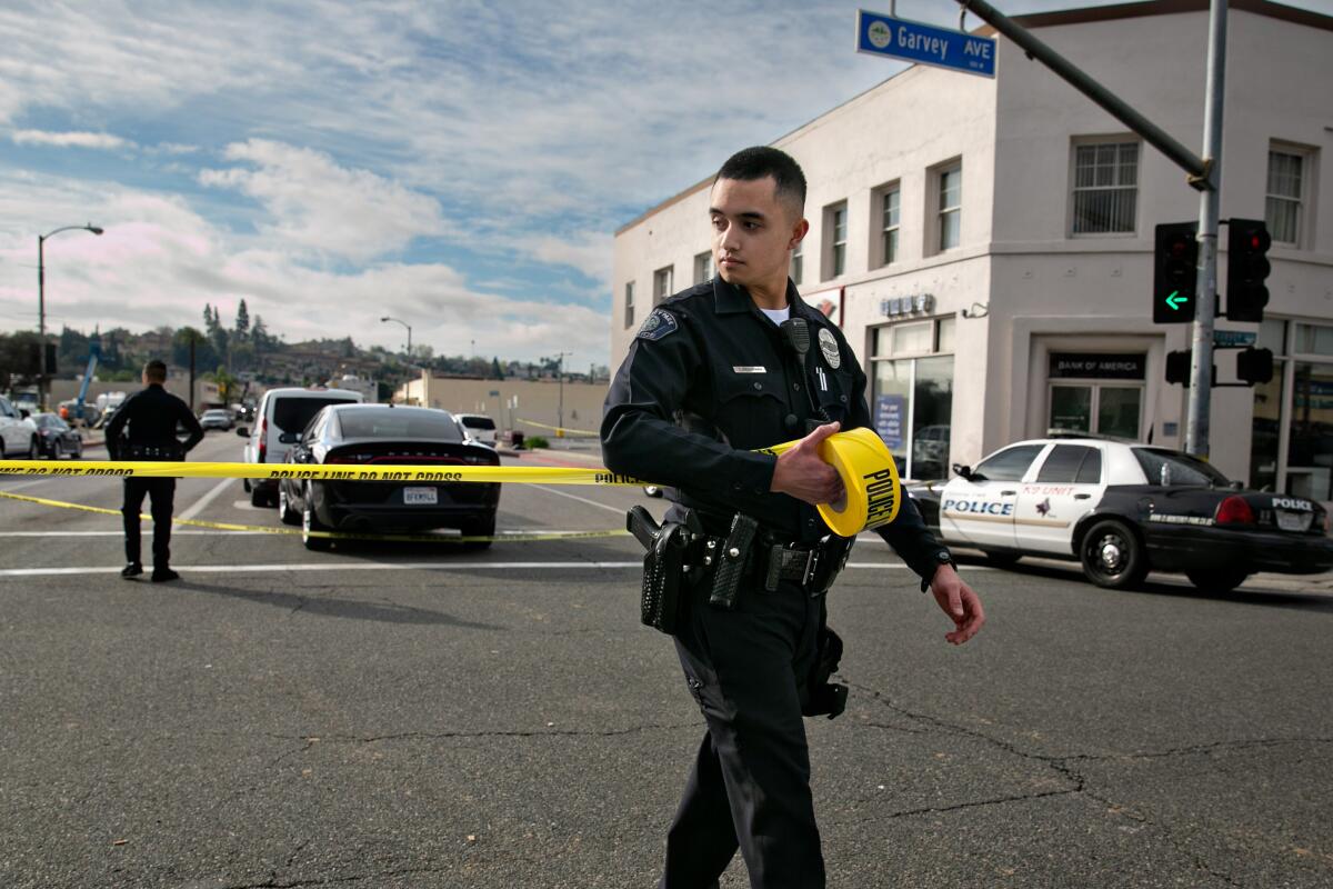 A police officer walks across a street unrolling police caution tape that says "police do not cross."