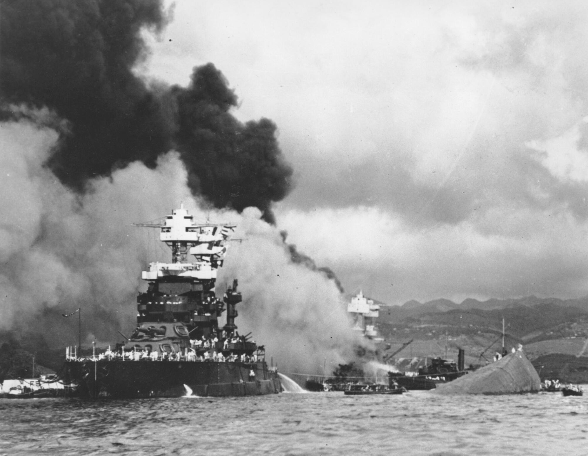 Huge, dark clouds of smoke billow behind a battle ship as part of another, capsized ship is seen on the right.