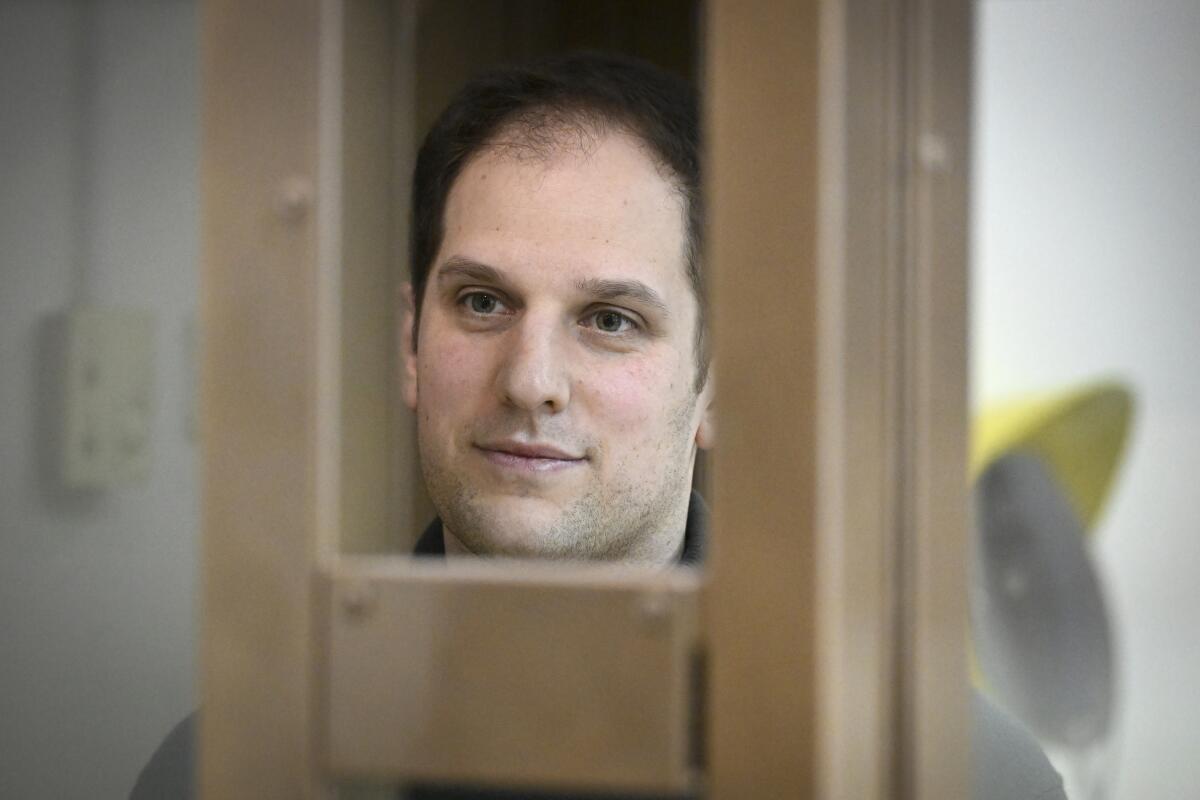 Evan Gershkovich stands in a glass cage in a courtroom