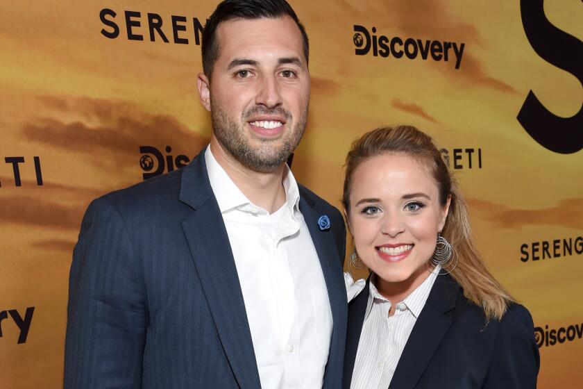 Jeremy Vuolo and Jinger Duggar Vuolo smile and pose together in dark blue suits.