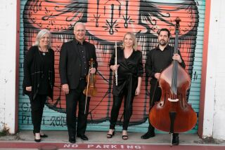 The Camarada Tango Quartet -- four musicians lined up in front of a mural.