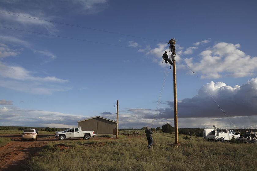 In this Wednesday, May 8, 2019 photo, utility workers prepare a power pole to connect a home in Kaibeto on the Navajo Nation to the electric grid. Miranda Haskie and her husband Jimmie Long Jr. have lived in the home with their son Jayden Long, 13, for more than a decade without electricity. An ambitious project to connect homes to the electric grid on the country's largest American Indian reservation is wrapping up. Utility crews from across the U.S. have volunteered their time over the past few weeks to hook up about 300 homes on the Navajo Nation. (AP Photo/Jake Bacon)