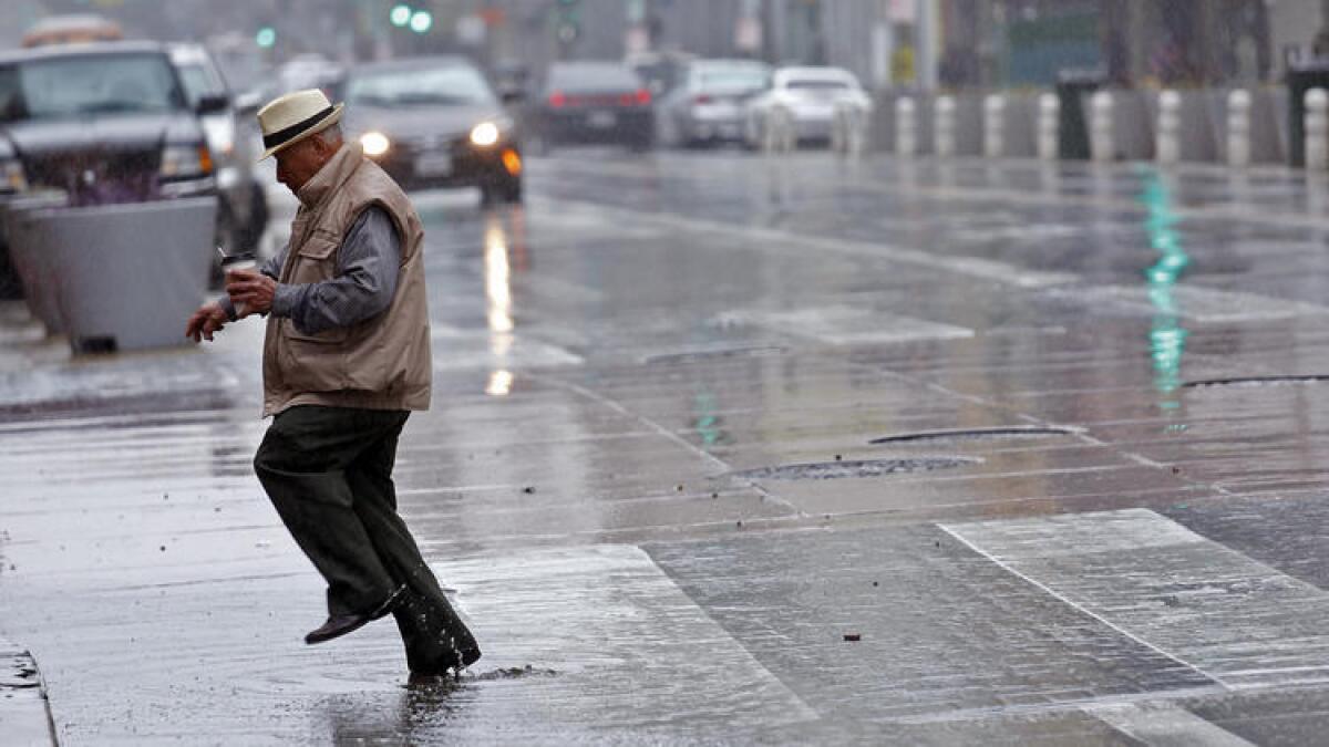 Un hombre brinca entre los charcos de la lluvia en la calle Broadway en el centro de Los Angeles.