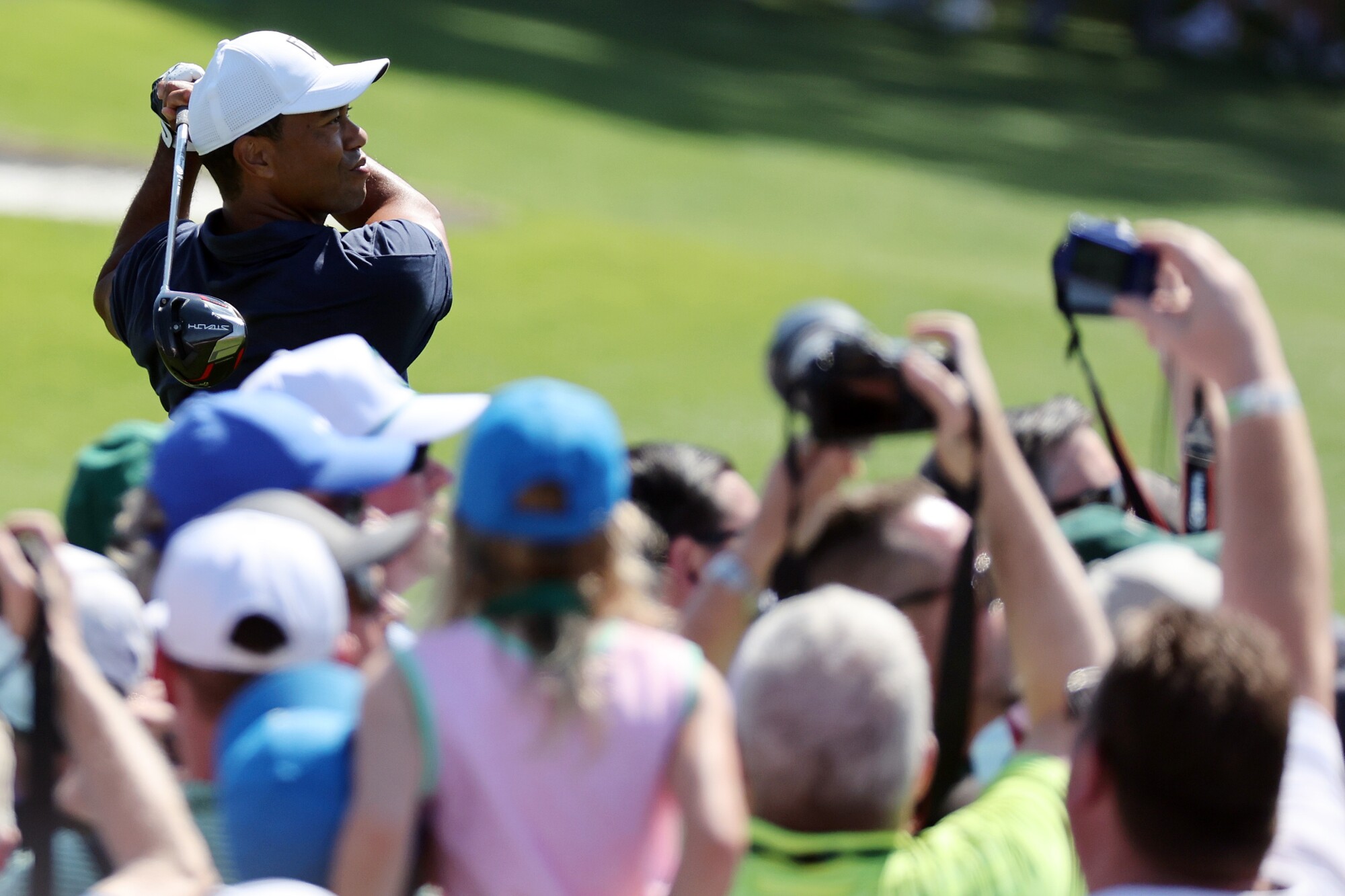 People take pictures as Tiger Woods swings a club