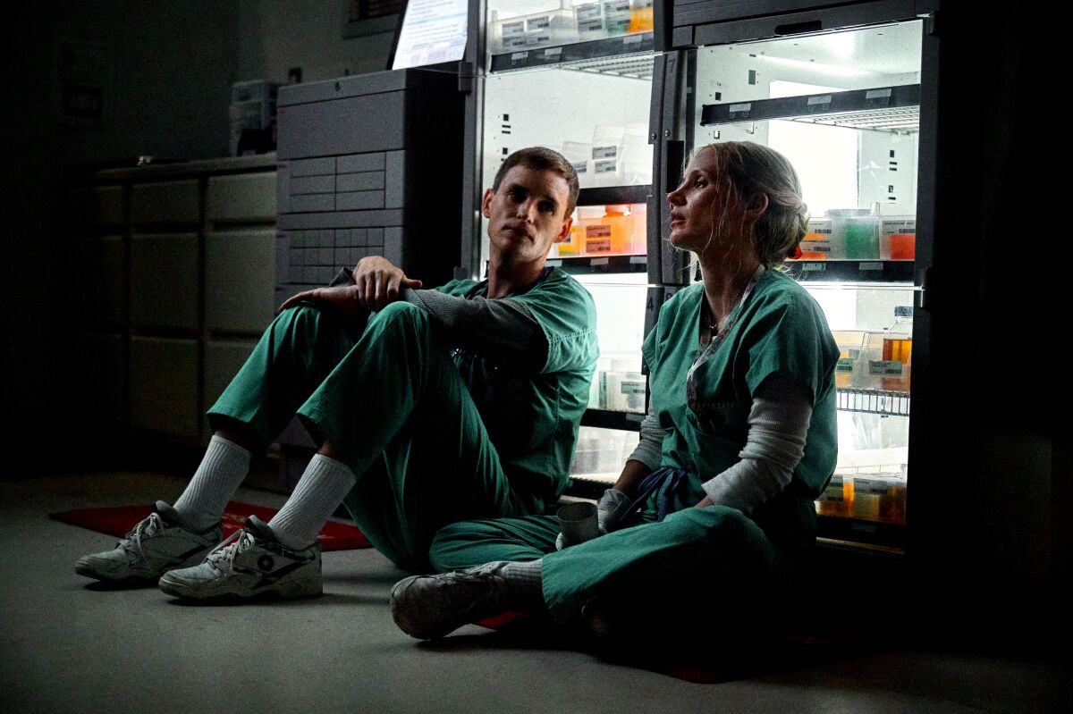 A male and female nurse wearing scrubs sit on the ground.