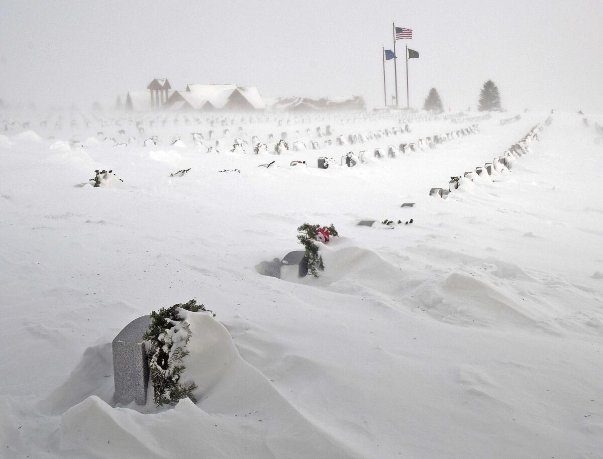 Deep snow blanketing a cemetery, leaving rows of headstones only partially visible.