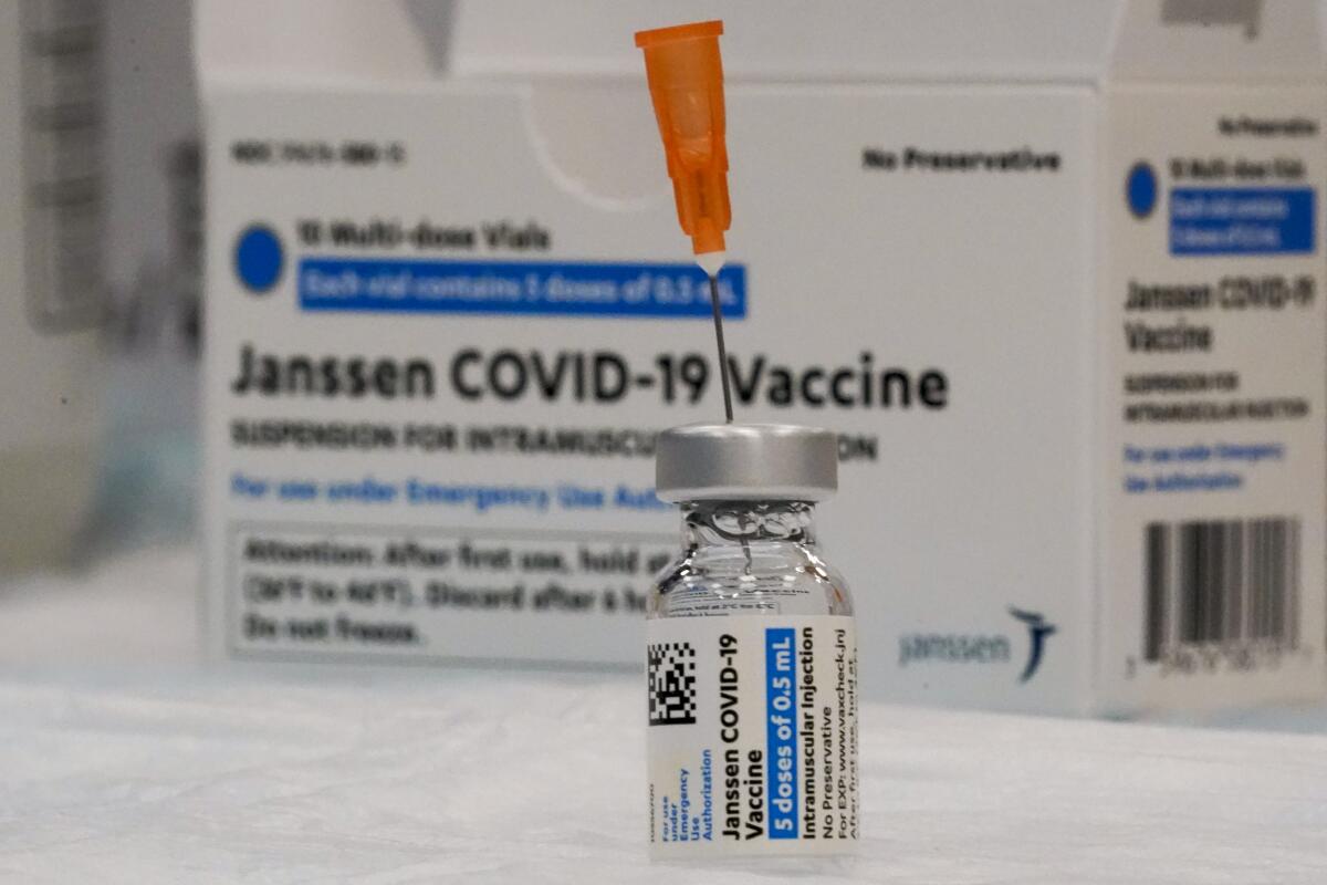A syringe needle pierces a vial of the Johnson & Johnson COVID-19 vaccine on a tray next to a box of vaccines.