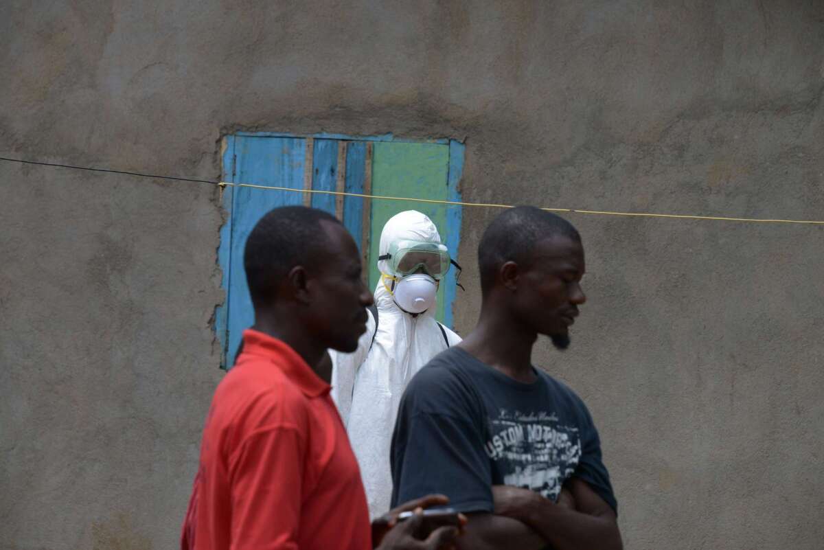 A medical worker with the Liberian Red Cross wears a protective suit while watching local residents in Banjol.