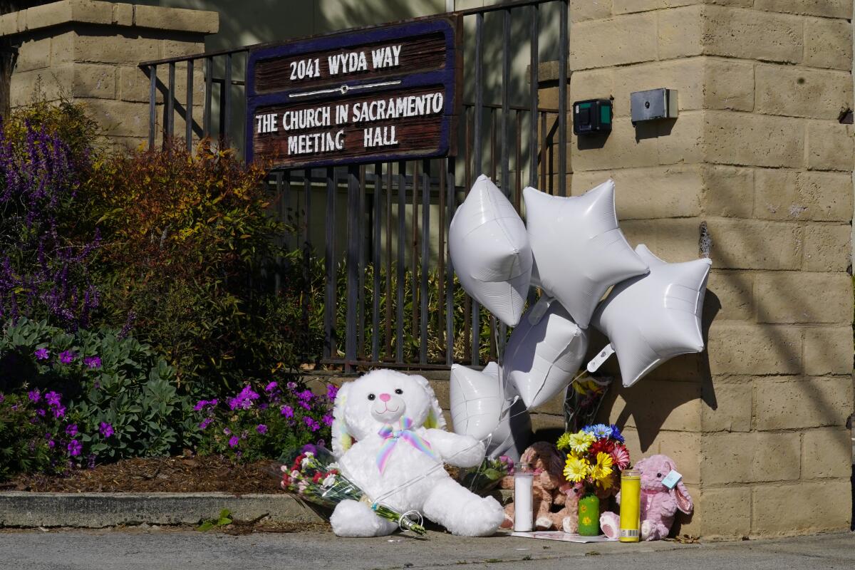 A teddy bear, balloons and flowers are among the items at a memorial in front of a church