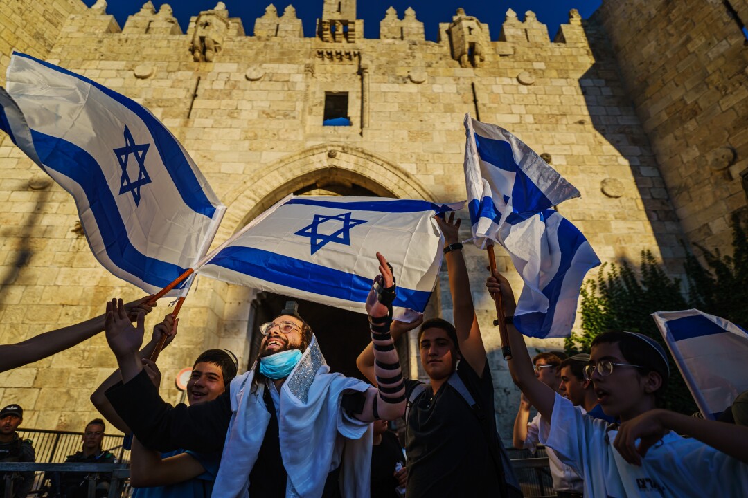 مردی در میان جمعیتی که پرچم های اسرائیل را به اهتزاز در می آورند ، دستان خود را در هوا بلند می کند.