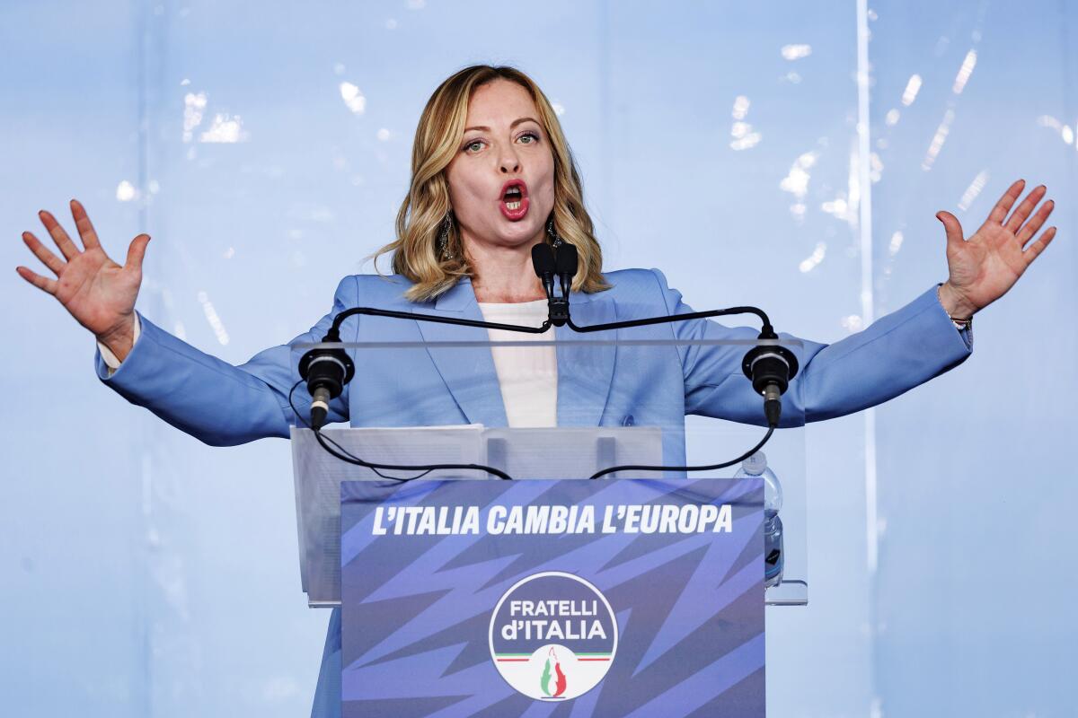 Italian Prime Minister Giorgia Meloni holds her arms out as she speaks at a lectern.