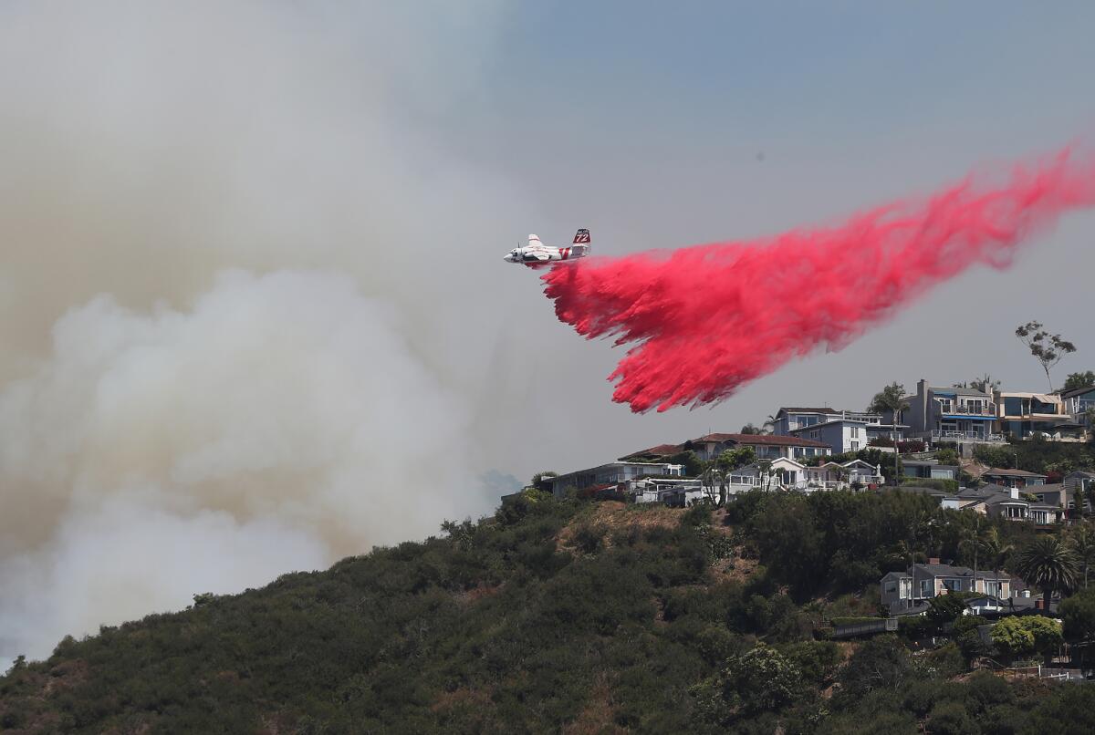 A Cal Fire firefighting plane drops fire retardant behind homes in the Arch Beach Heights neighborhood of Laguna Beach.