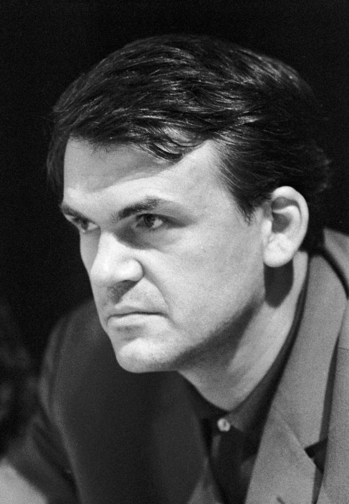A black and white photo of Milan Kundera from 1967 wearing a blazer and leaning forward.