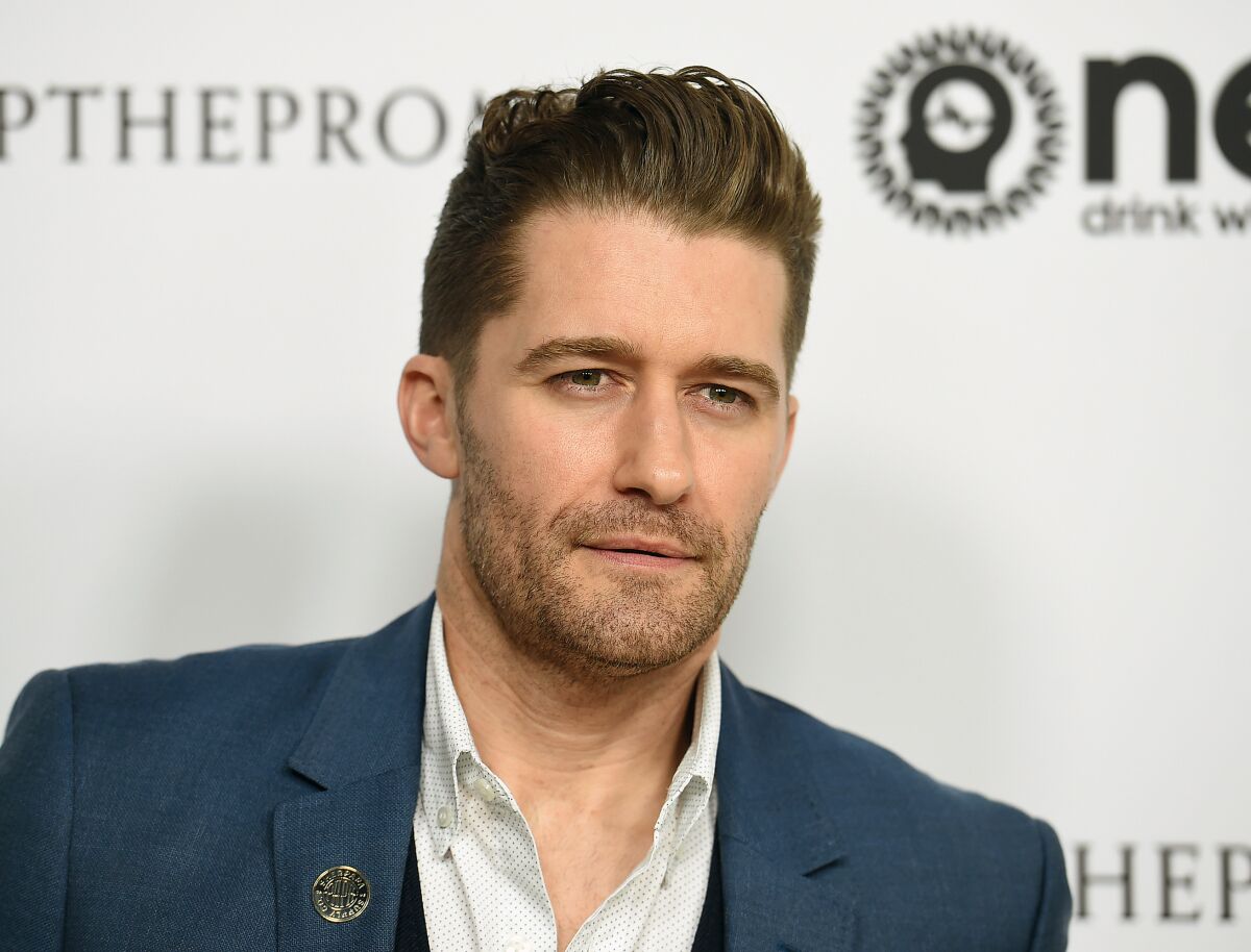 A man with a faint beard looks stoic posing at a red carpet event