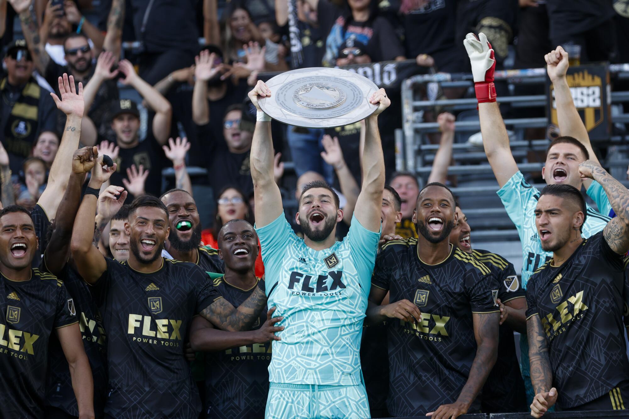 LAFC goalkeeper Maxime Crepeau holds up the Supporters' Shield trophy and smiles while celebrating with teammates