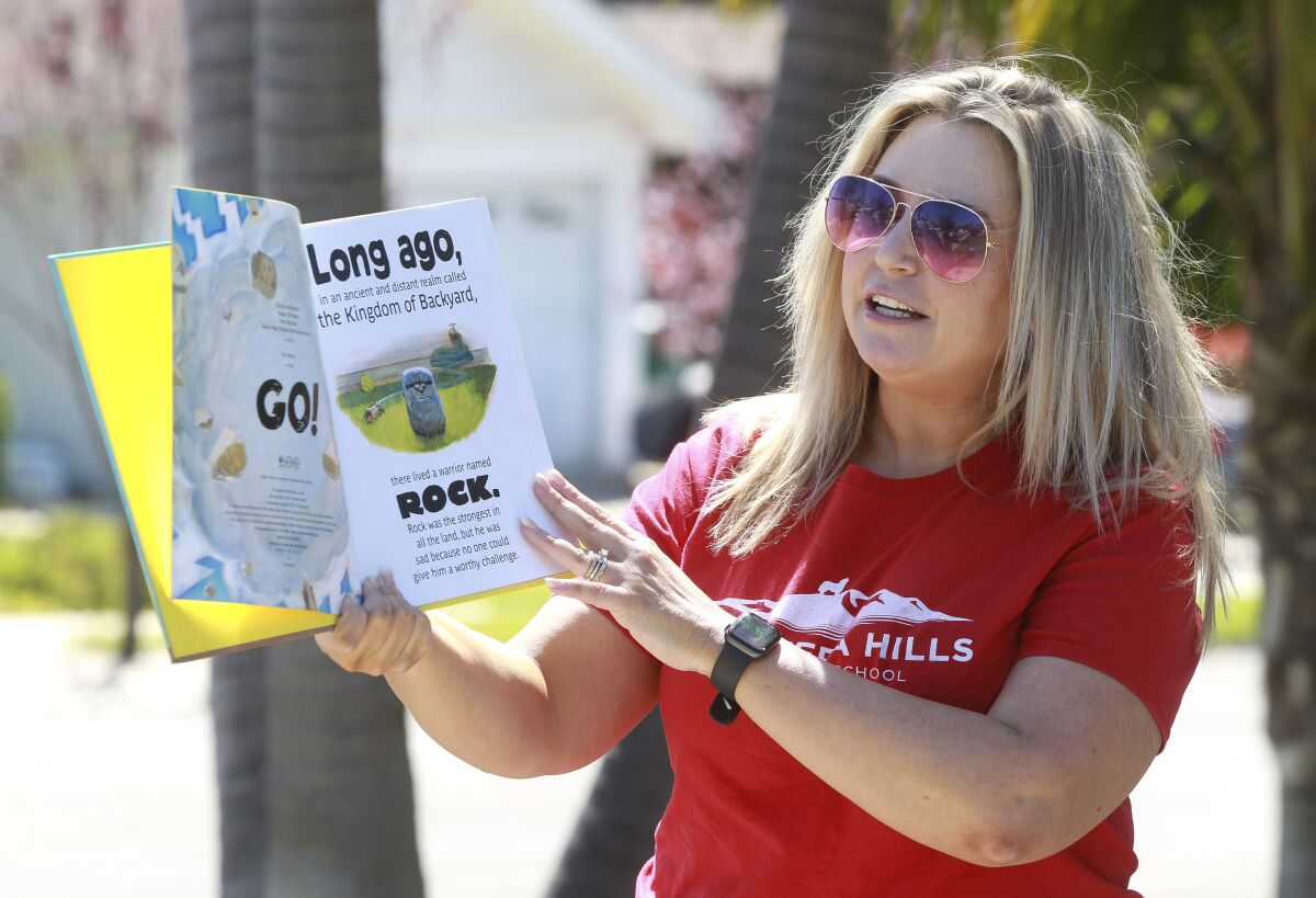 Library Media Technician for Calavera Hills Elementary School Lindsay Rudy reads "The Legend of Rock, Paper, Scissors" to children while in front of their home on Friday March 27, 2020 in Carlsbad, California.
