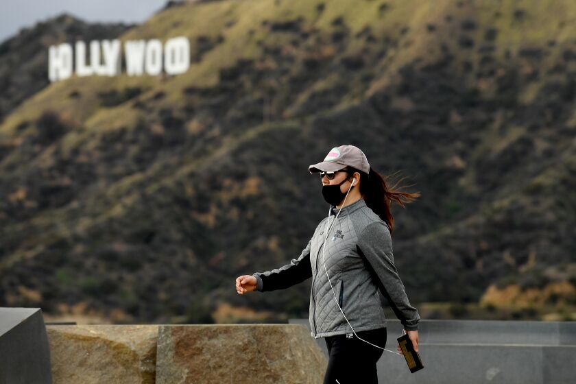 LOS ANGELES, CALIFORNIA MARCH 23, 2020-A hiker wearing a mask because of the coronavirus walk past the Hollywood sign in Griffith Park Monday. (Wally Skalij/Los Angeles Times)